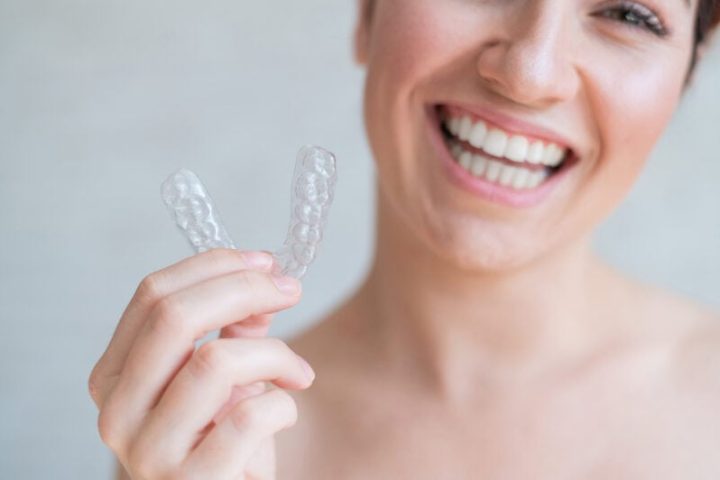 Close-up of orthodontic silicone transparent teeth aligner in female hands. A woman with a perfect charm smile holds a removable night retainer. Bracket for teeth whitening. Cropped photo