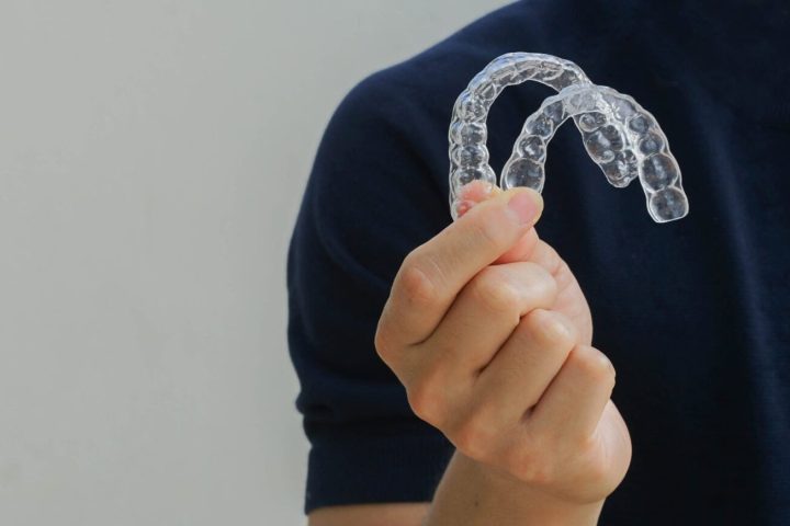 close up man hand holding dental aligner retainer (invisible) on  background for beautiful teeth treatment course concept