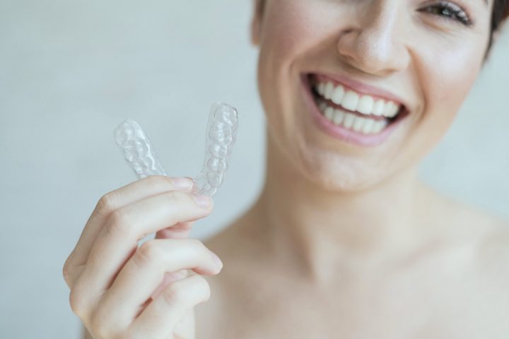 Close-up of orthodontic silicone transparent teeth aligner in female hands. A woman with a perfect charm smile holds a removable night retainer. Bracket for teeth whitening. Cropped photo